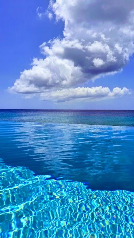 Clear turquoise pool water meeting the Caribbean sea beneath dramatic clouds